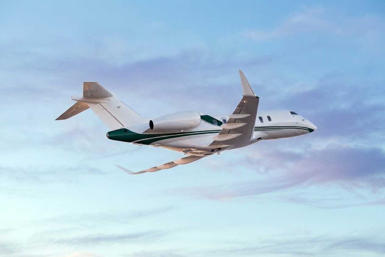 White business jet with dark green accents flying above the clouds against a bright blue sky, viewed from below in mid-flight.