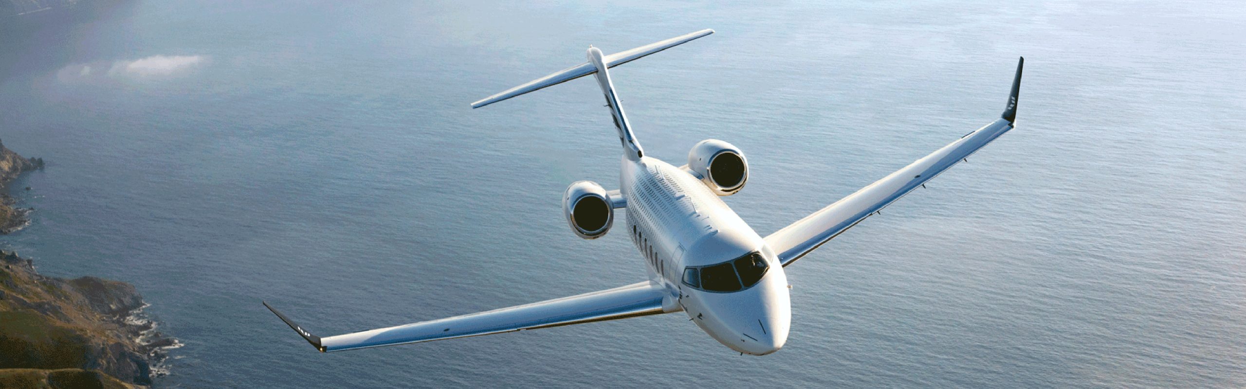 Bombardier Challenger 650 aircraft in flight over a coastal landscape.