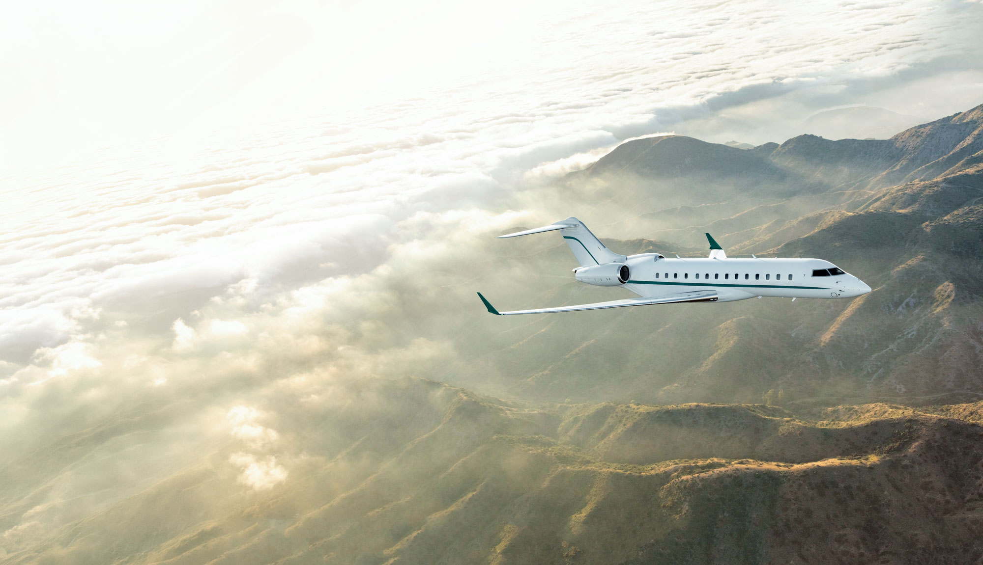 White private jet with a continuous dark green stripe beneath the cabin windows and matching green tail accents, flying above sunlit mountain peaks and a sea of clouds.