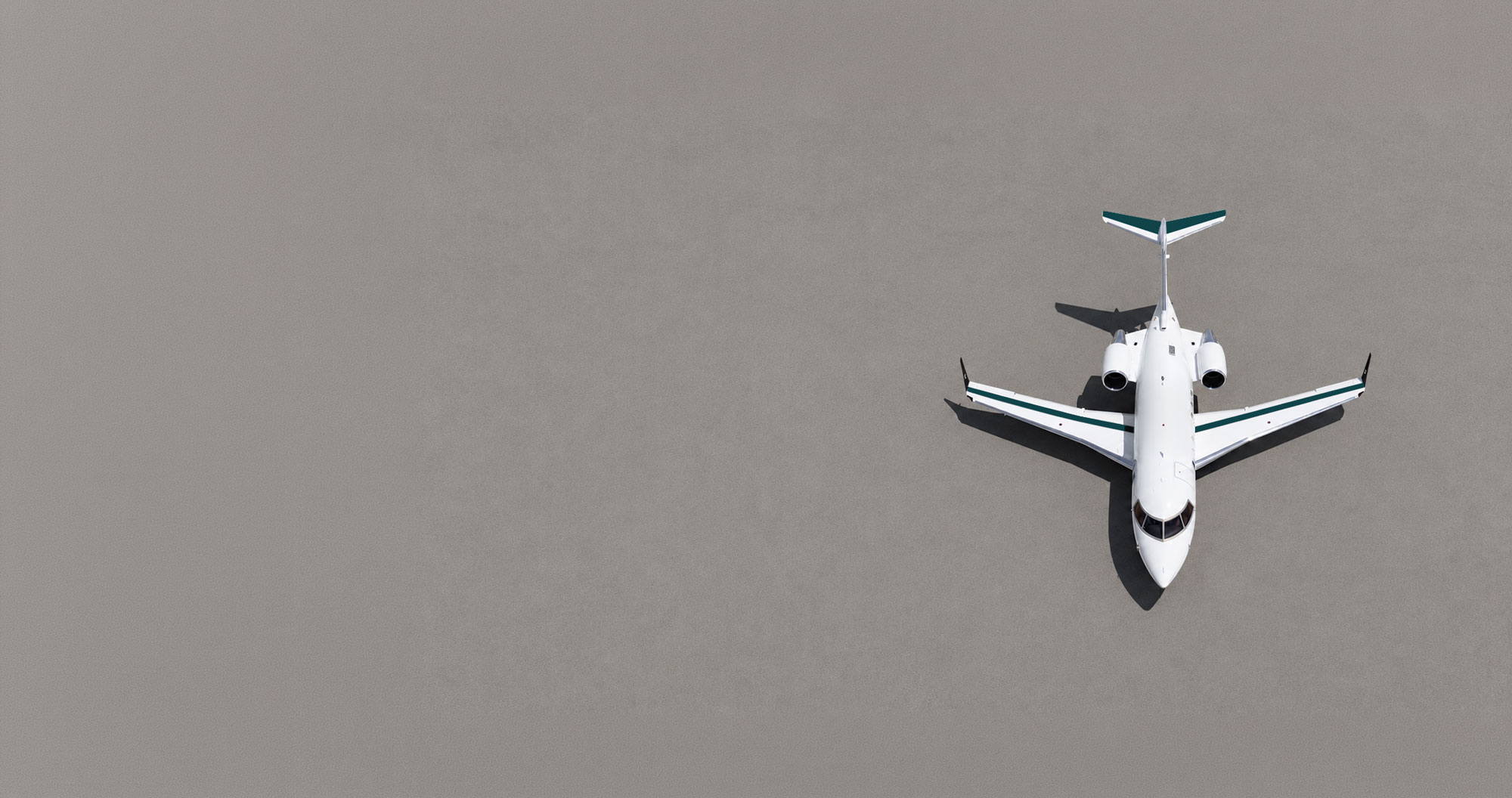 Top-down aerial view of a white Bombardier Challenger 650 business jet positioned on a runway threshold with bold white centerline markings. The aircraft is centered in the frame, creating a clean, symmetrical composition with expansive negative space on the left, emphasizing precision, performance, and modern business aviation.