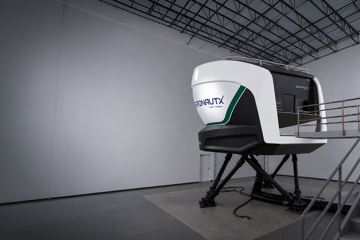 Advanced full-flight simulator inside a modern aviation training facility. The white simulator cabin with green AeronautX branding is mounted on a full-motion platform with hydraulic actuators, while a staircase and access platform lead to the cockpit entrance. The bright, spacious training hall highlights state-of-the-art flight simulation technology used for professional pilot training and certification.